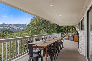 A covered outdoor dining area with a long table and chairs, overlooking a hilly landscape. - The Retreat at Mount Taylor, by Vinifera Homes (Santa Rosa)