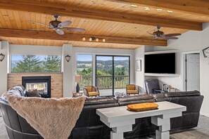A modern living room with a fireplace, leather sofas, a dining table, and a TV mounted on the wall. - The Retreat at Mount Taylor, by Vinifera Homes (Santa Rosa)