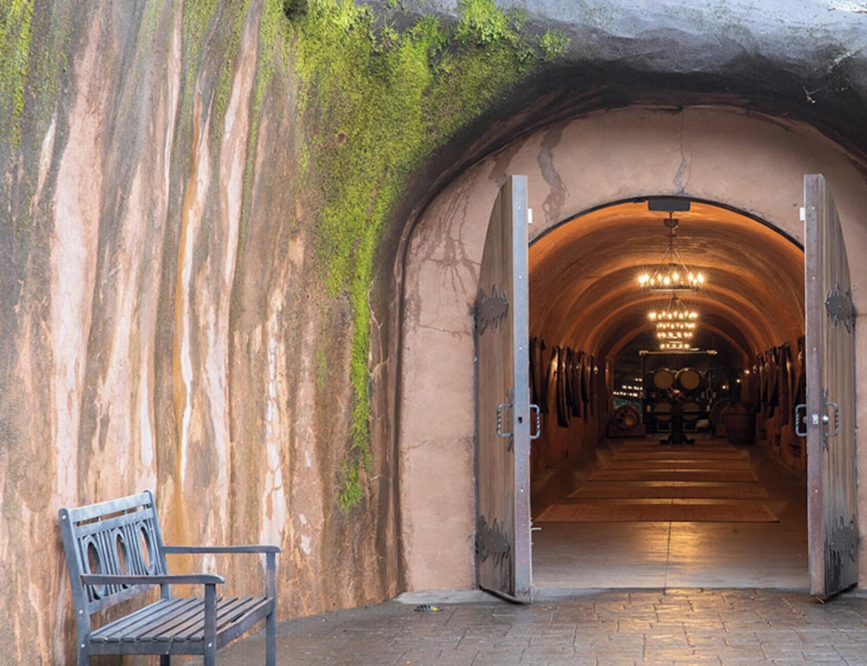 A tunnel entrance with a bench outside, leading to a room with a chandelier and musical instruments.