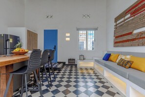 Een knus woongedeelte met een keuken, een eettafel met stoelen, een bank met kussens en een zwart-wit geruite vloer.
