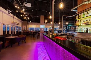 A bar area with a counter, seating, and a view through the windows. - Premier Inn Dubai Ibn Battuta Mall (Dubai)