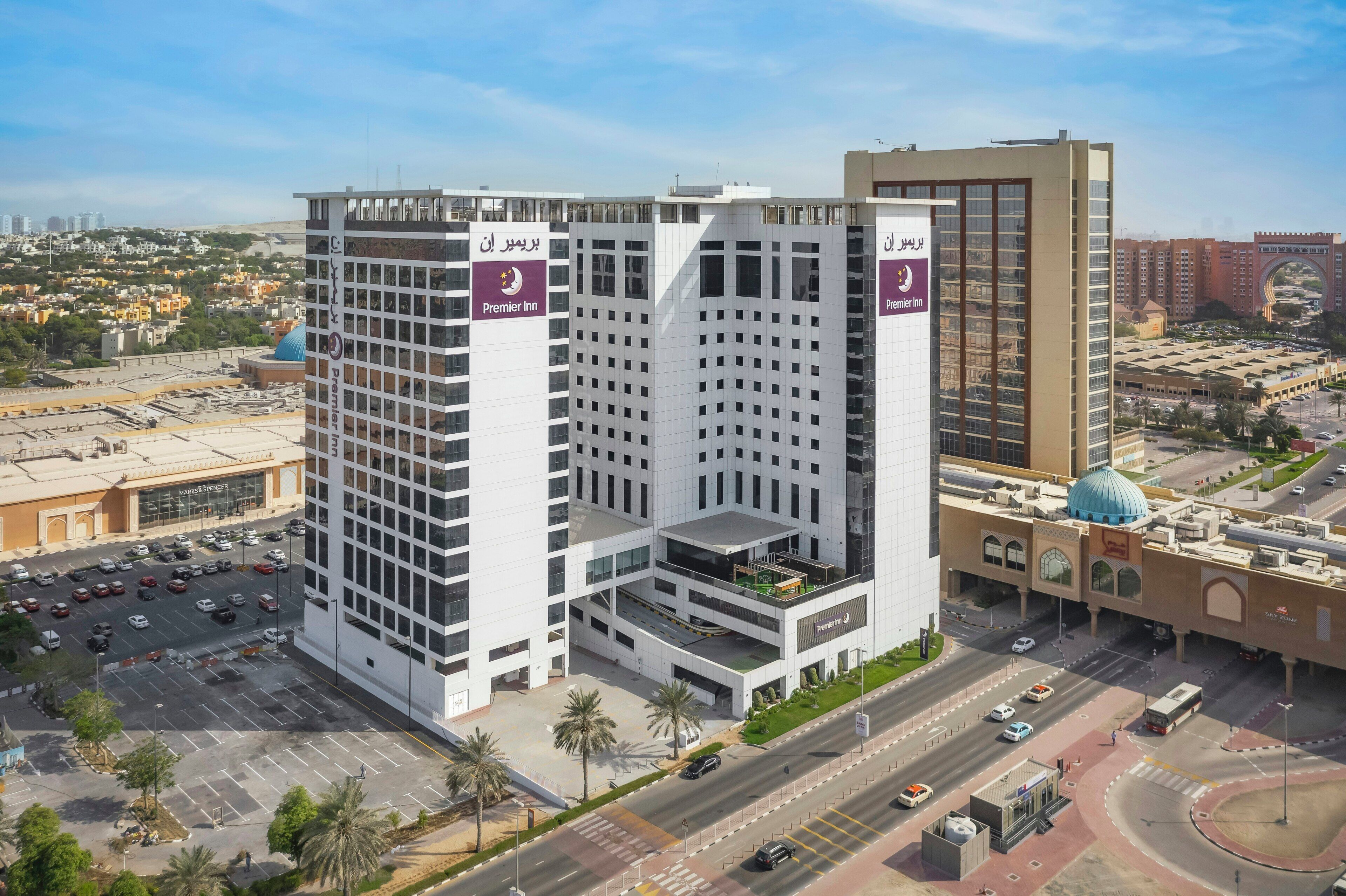 A multi-story hotel with a prominent Premier Inn sign, surrounded by a parking area and a busy road.