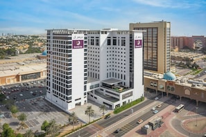 A multi-story hotel with a prominent Premier Inn sign, surrounded by a parking area and a busy road. - Premier Inn Dubai Ibn Battuta Mall (Dubai)