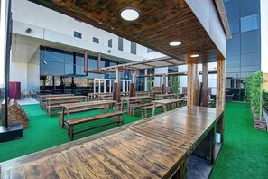 An indoor dining area with wooden tables and benches, a green carpet, and a modern building exterior. - Premier Inn Dubai Ibn Battuta Mall (Dubai)