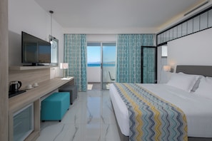 A modern hotel room with a bed, a desk with a computer, a television, and a view of the sea. - Sunrise Beach Resort (Rhodes)