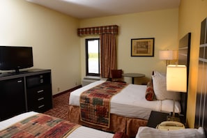 Habitación de hotel con cama, escritorio con televisor, silla, lámpara y ventana con cortinas.