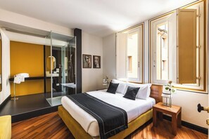 A hotel room with a bed, a mirror, a small table with a vase, and a bathroom visible through a glass door. - Ferrara Hotel (Ferrara)