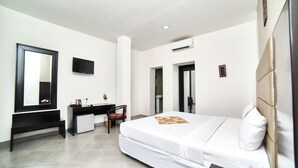 A modern hotel room with a large bed, a desk, a chair, a flat-screen TV, and an air conditioning unit.