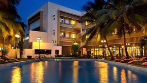 A hotel with a swimming pool, palm trees, and a multi-story building with balconies.