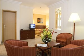 A hotel room with a bed, a television, a desk with a lamp, and two armchairs.