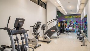 A gym with various exercise machines, a wall mural, and a ceiling with recessed lighting.