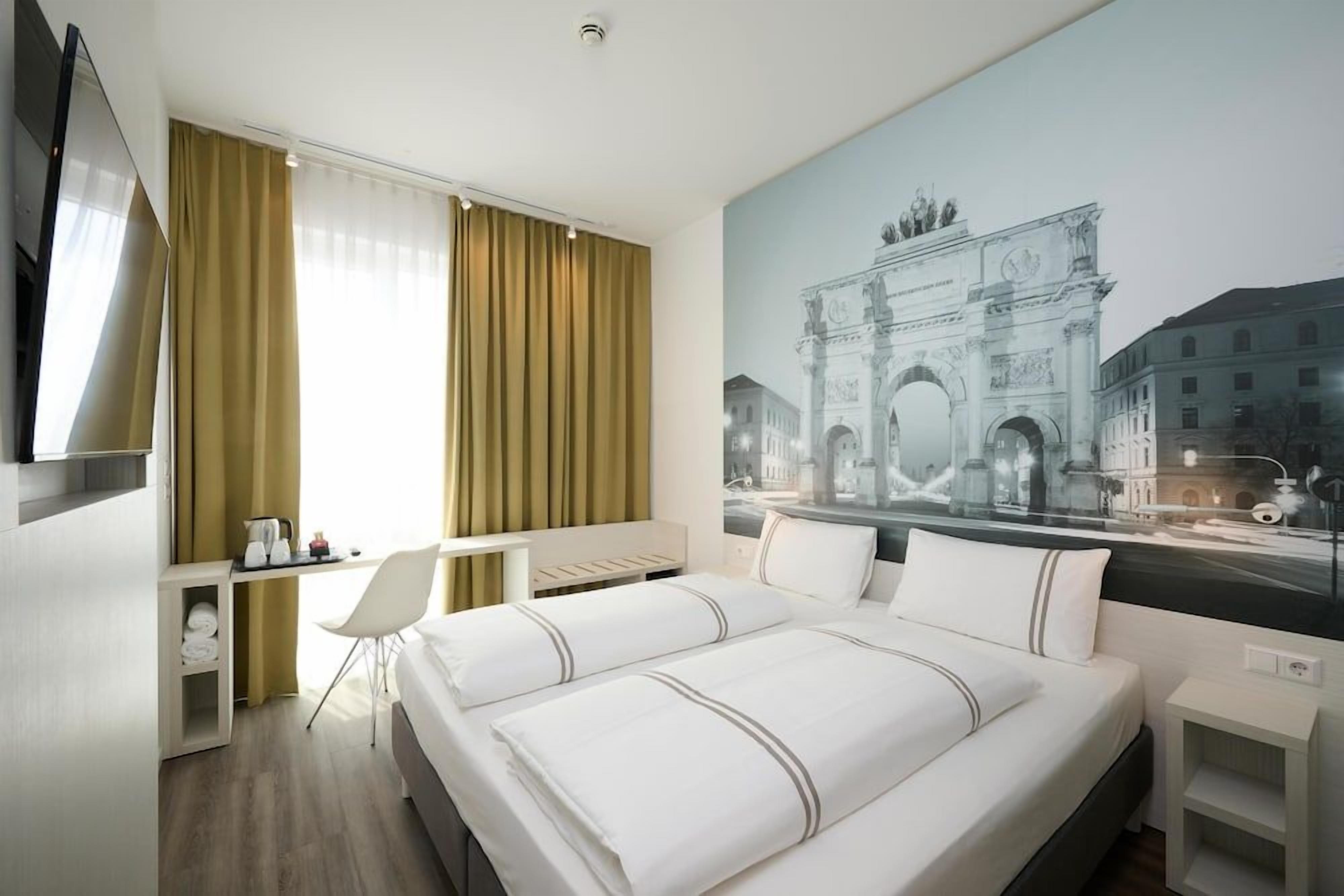 Una habitación de hotel con cama, escritorio, silla y una ventana grande.