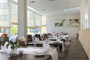 Een restaurant met gedekte tafels, witte tafelkleden, glazen en bloemstukken.