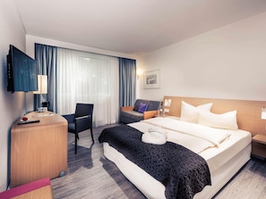 A hotel room with a bed, a desk, a chair, a TV, and a window with curtains. - Mercure Hotel Saarbrucken Sud (Saarbrücken)