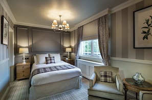 A bedroom with a large bed, two bedside tables, a chair, a window with curtains, a chandelier, and a framed botanical print on the wall. - Down Hall Hotel Spa & Estate (Bishop's Stortford)
