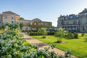 A courtyard with a pathway, surrounded by well-maintained lawns and flowering trees. - Down Hall Hotel Spa & Estate (Bishop's Stortford)
