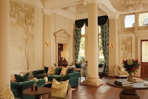Een ruime lobby met een groene zithoek, een ronde salontafel en een grote kolom.