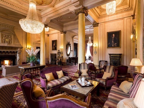 A luxurious lobby with ornate columns, plush seating, a fireplace, and elegant chandeliers. - Down Hall Hotel Spa & Estate (Bishop's Stortford)