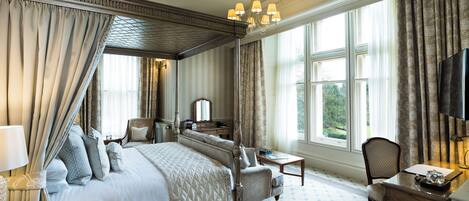 A four-poster bed with a canopy, a desk with a chair, a television, and a large window with curtains.
