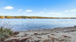 Ein See mit sandigem Ufer und Bäumen im Hintergrund.