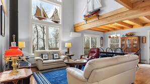 Ein geräumiges Wohnzimmer mit hohen Decken, großen Fenstern, einem Kamin und einem Essbereich mit Stühlen und einem Tisch.