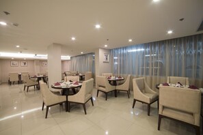 Ein Hotelrestaurant mit mehreren runden Tischen und Stühlen, einem großen Fenster mit Vorhängen und einem sauberen, modernen Interieur.