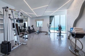 A modern gym with various exercise equipment, a treadmill, and a view of the ocean. - Razana Hotel Al Jubail (Al Jubail)