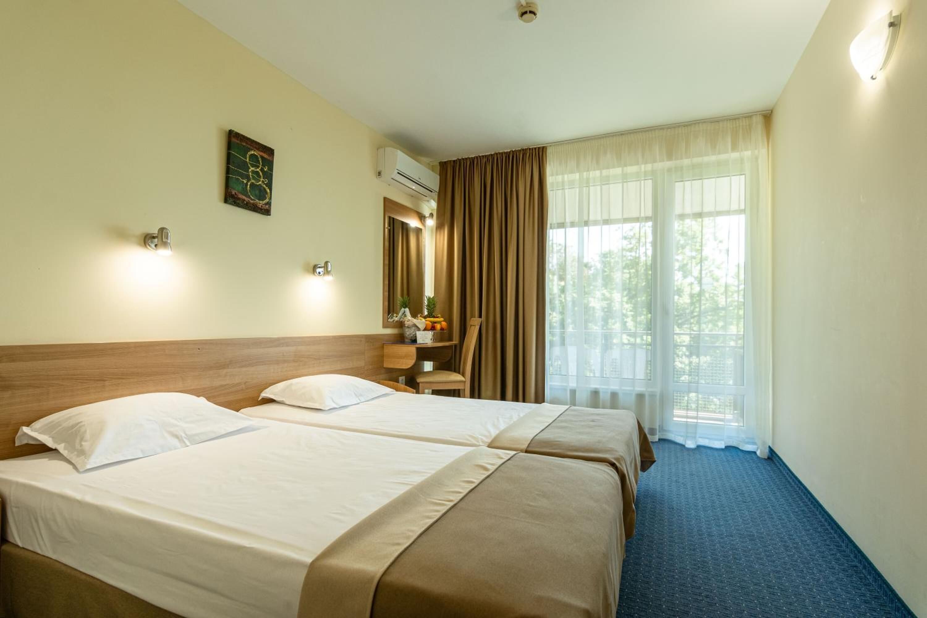 A hotel room with two beds, a desk, a chair, an air conditioning unit, and a window with curtains.