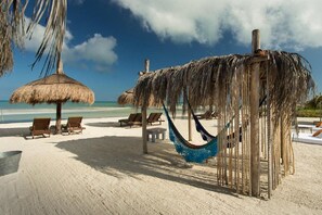 Ein Strand mit Reetdachschirmen, Holzliegestühlen und einer Hängematte.