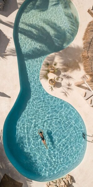 A unique infinity pool with a person swimming, surrounded by lounge chairs and palm trees. - Ser Casasandra Boutique Hotel (Isla Holbox)