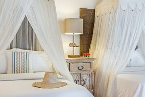 Quarto com cama de dossel, luminária de cabeceira, cesto de vime e uma pequena mesa com flores.