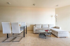 A modern living room with a glass dining table, two white chairs, a grey sofa, and a floor lamp. - Garden OF Eden Complex (Nessebar)