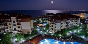Zona residencial con varios edificios de apartamentos, una piscina y vistas al mar de noche.