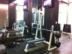 A gym with weightlifting equipment, a bench, and a television on the wall. - Garden of Eden Complex (Nessebar)