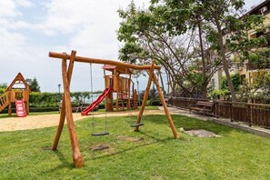 A playground with swings and a slide, surrounded by grass and trees. - Garden of Eden Complex (Nessebar)