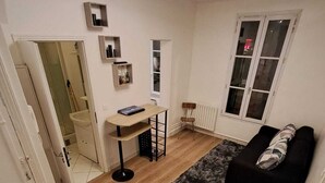 Un espace de vie compact comprenant un canapé, une petite table, un radiateur et une fenêtre.