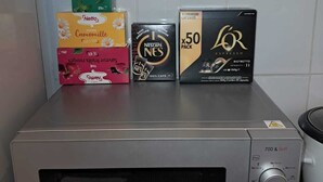 Une cuisine équipée d’un four à micro-ondes, d’une machine à café et de différentes capsules de café disposées sur le comptoir.