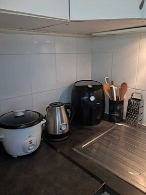 A kitchen with a slow cooker, electric kettle, coffee maker, and utensils.
