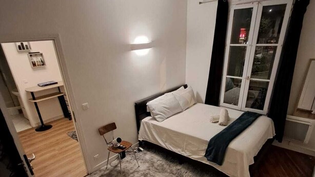 Une chambre à coucher avec un lit, une fenêtre avec des rideaux, une table de chevet et une chaise.
