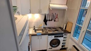 Une cuisine compacte avec des meubles blancs, une cuisinière encastrée, un lave-linge et une fenêtre donnant sur un beau paysage.