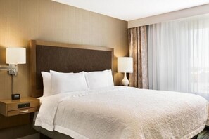 A hotel room with a large bed, two bedside tables, a nightstand, and a window with curtains.