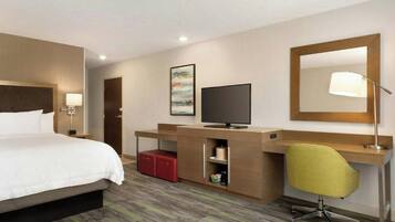 A hotel room with a bed, desk, television, and a mirror.