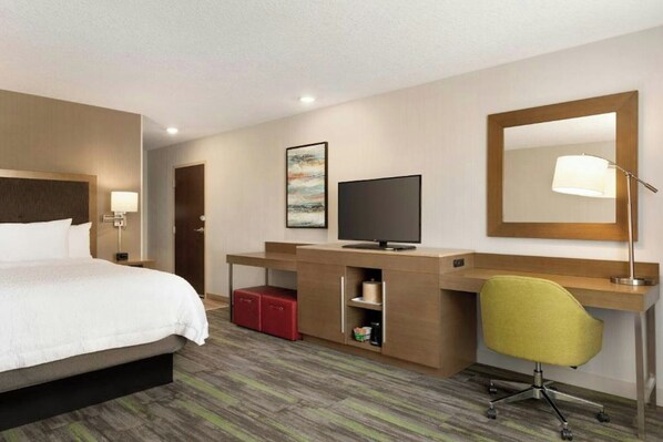 Una habitación de hotel con cama, escritorio, televisor y espejo.
