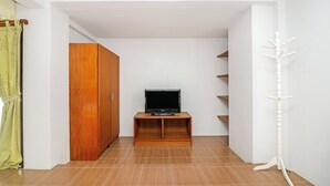 A room with a television on a wooden stand, a wardrobe, and a coat rack. - Eco Hostel (Hua Hin)