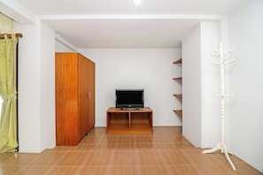 Habitació amb televisió sobre un prestatge de fusta, un armari i una perxa.