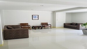 A spacious living room with a large sofa, two wooden chairs, a coffee table, and a potted plant. - Eco Hostel (Hua Hin)