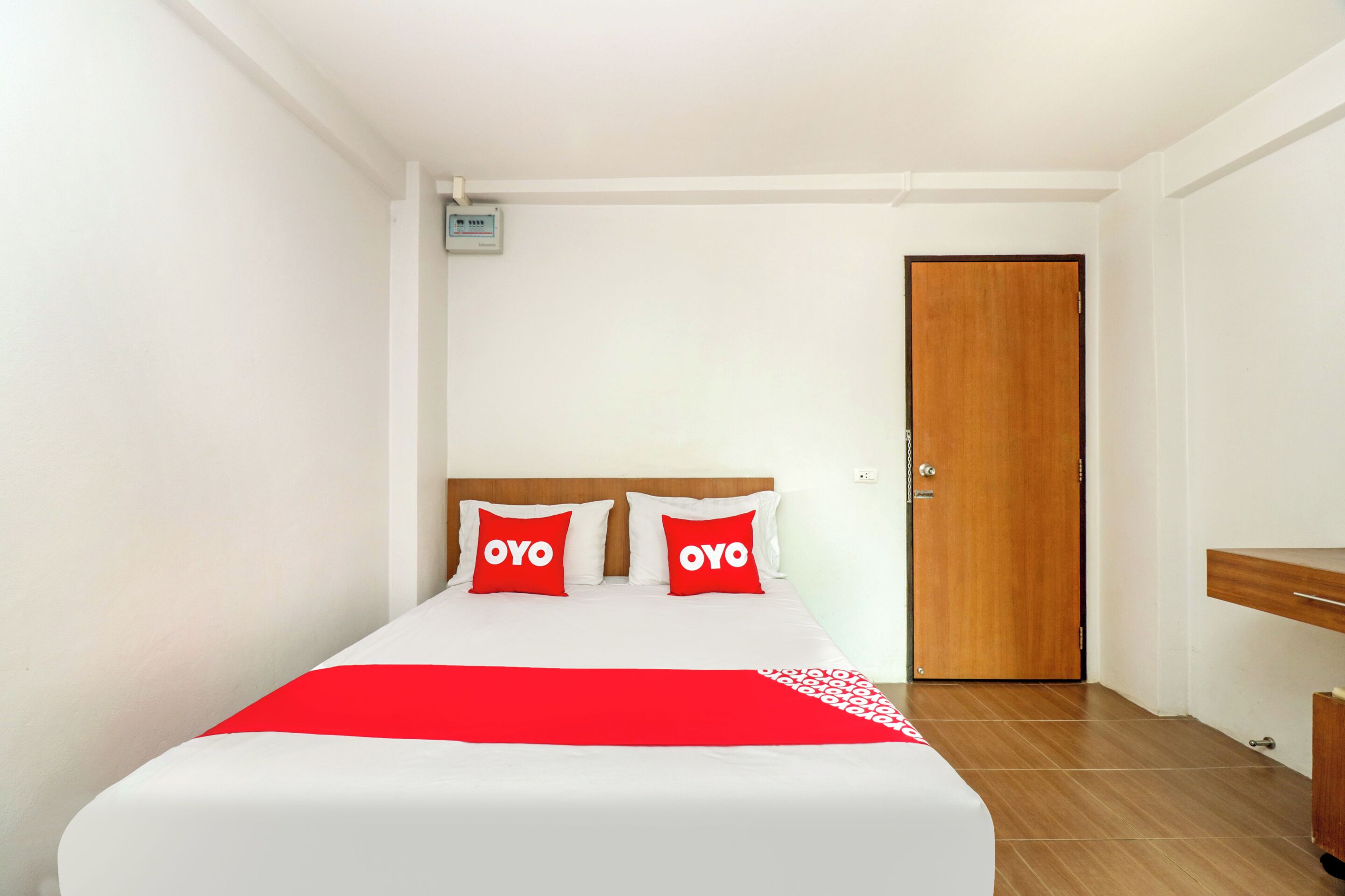 Ein Hotelzimmer mit einem Bett, zwei roten Kissen, einer Holztür und einem kleinen weißen Schild an der Wand.