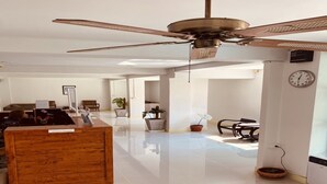 A spacious hotel lobby with a wooden reception desk, a ceiling fan, and a clock on the wall. - Eco Hostel (Hua Hin)