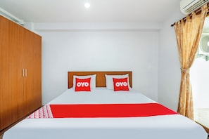 Habitació d'hotel amb llit, armari de fusta i finestra amb cortines.