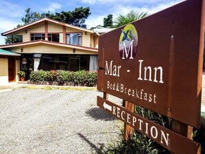 Segnaletica di Mar Inn con area reception, un edificio dalla facciata beige e una zona verde con piante.